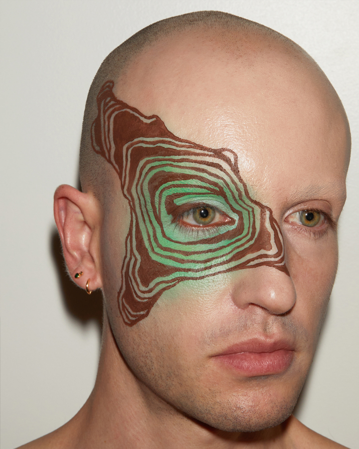 Jesse Clark posing blue and white cloud facepaint on against a sky blue background.